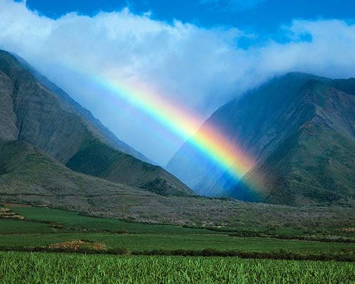 A rainbow is seen in the sky over mountains.