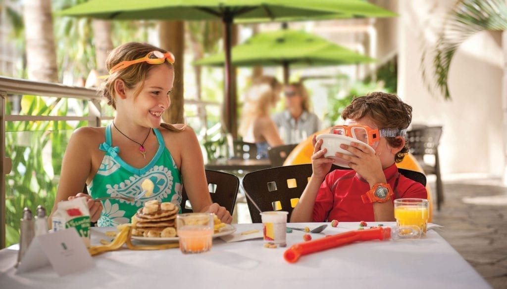 Two children sitting at a table with food.