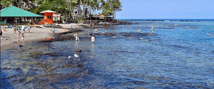 A group of people swimming in the ocean, enjoying a sunny day near a sandy beach. Waves gently lap at the shore.