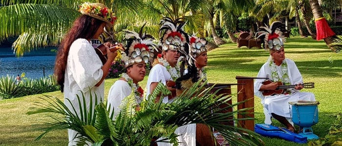 Cruise to Hawaii from Tahiti. A group of people in white shirts and feathers on their heads.